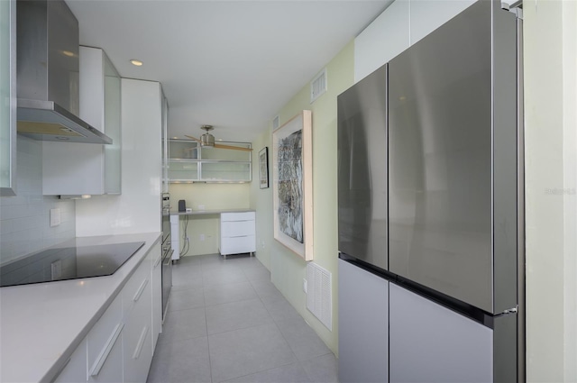 kitchen featuring visible vents, freestanding refrigerator, black electric cooktop, wall chimney range hood, and backsplash