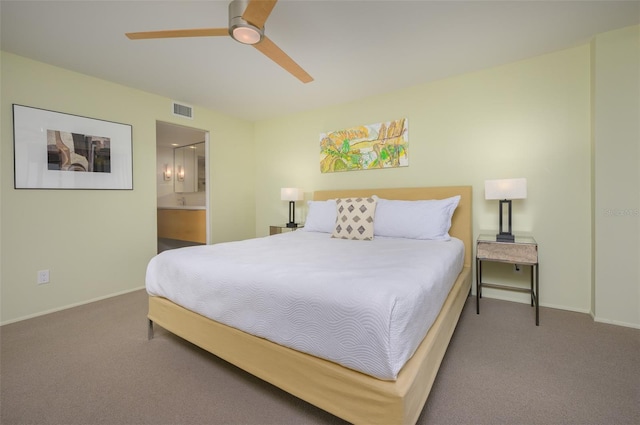 carpeted bedroom featuring ceiling fan, ensuite bath, visible vents, and baseboards