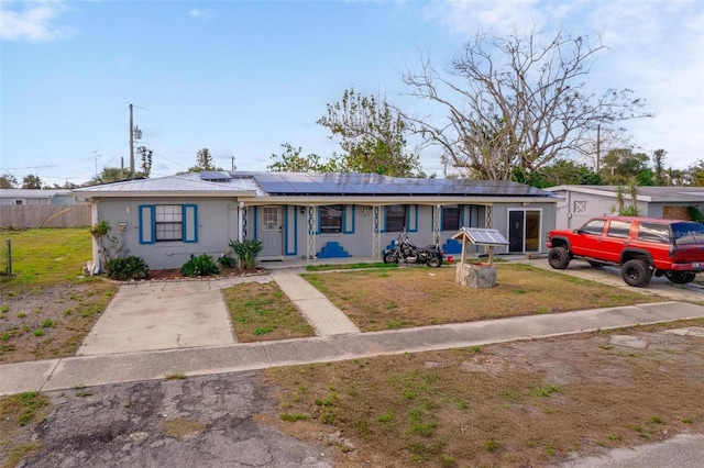 ranch-style home featuring stucco siding, a front yard, roof mounted solar panels, fence, and metal roof