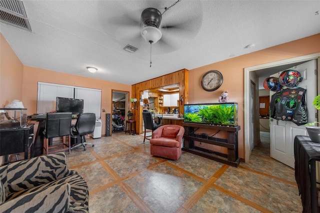 living area featuring baseboards, ceiling fan, visible vents, and a textured ceiling