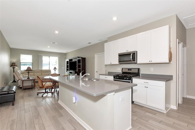 kitchen with light wood-type flooring, stainless steel appliances, an island with sink, sink, and white cabinetry