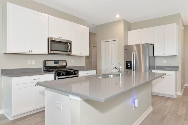 kitchen with appliances with stainless steel finishes, an island with sink, light stone countertops, sink, and white cabinetry