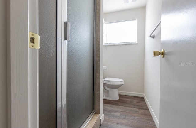 bathroom featuring wood-type flooring, toilet, and a shower with door