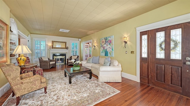 living room with visible vents, baseboards, wood finished floors, and a glass covered fireplace