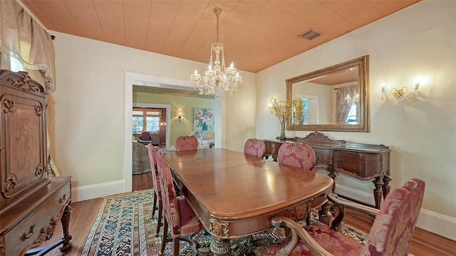 dining area featuring baseboards, visible vents, a chandelier, and wood finished floors