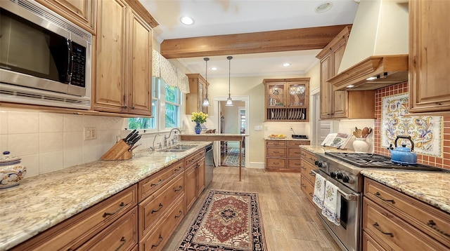 kitchen with light wood-style flooring, custom range hood, light stone counters, stainless steel appliances, and a sink