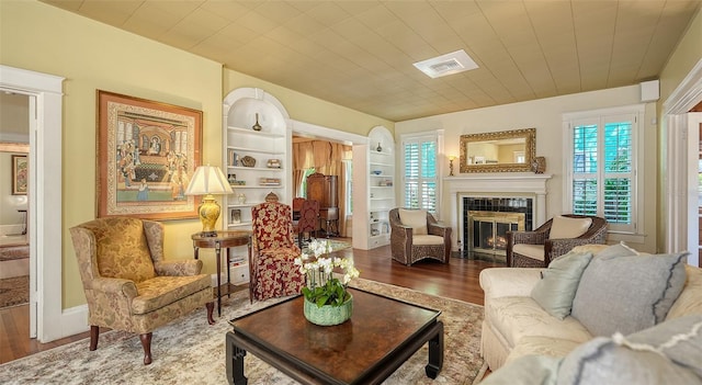 living area featuring a tiled fireplace, visible vents, built in features, and wood finished floors