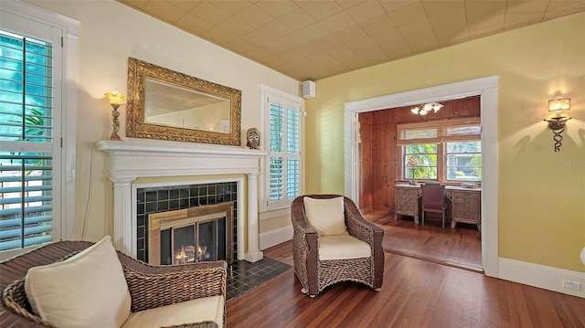 living area with a tiled fireplace, baseboards, an inviting chandelier, and wood finished floors