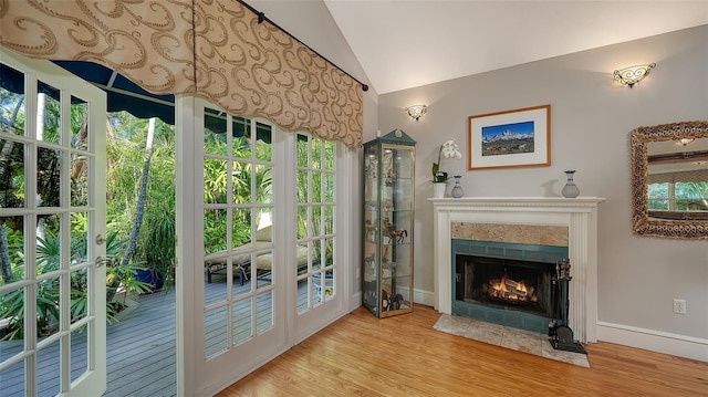 interior space featuring a fireplace with flush hearth, baseboards, vaulted ceiling, and wood finished floors