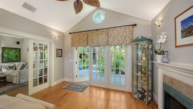 doorway to outside featuring a ceiling fan, visible vents, high vaulted ceiling, a high end fireplace, and wood finished floors