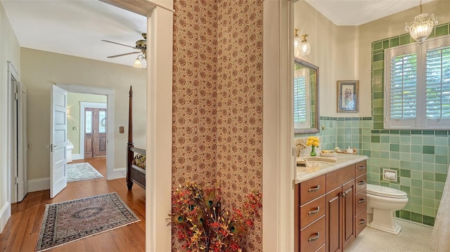 bathroom with ceiling fan, vanity, toilet, wood finished floors, and tile walls