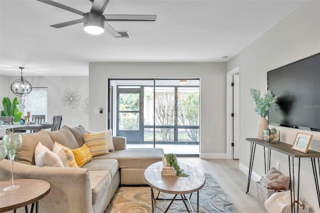 living room featuring ceiling fan with notable chandelier, a healthy amount of sunlight, and light hardwood / wood-style flooring