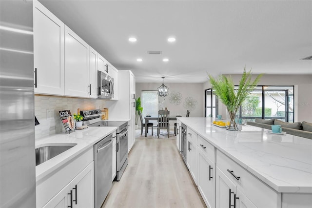 kitchen featuring decorative backsplash, white cabinets, stainless steel appliances, and light stone counters