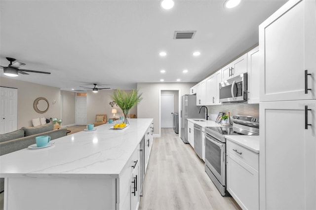 kitchen featuring white cabinetry, a center island, light hardwood / wood-style floors, light stone counters, and appliances with stainless steel finishes