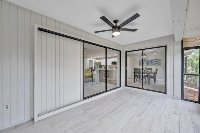 empty room featuring ceiling fan with notable chandelier and light wood-type flooring