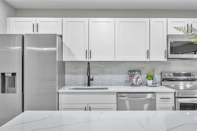 kitchen with stainless steel appliances, light stone countertops, white cabinets, backsplash, and sink