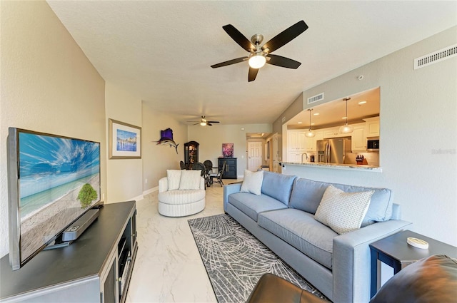 living area with a textured ceiling, marble finish floor, visible vents, and a ceiling fan