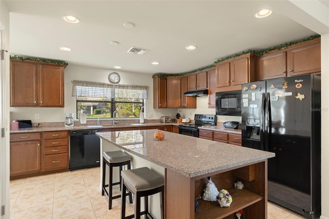 kitchen with a center island, a breakfast bar, black appliances, light stone countertops, and sink