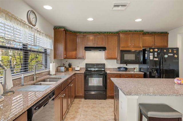 kitchen featuring a kitchen breakfast bar, light stone counters, black appliances, light tile patterned flooring, and sink