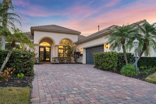 view of front of home with decorative driveway, french doors, a garage, and stucco siding