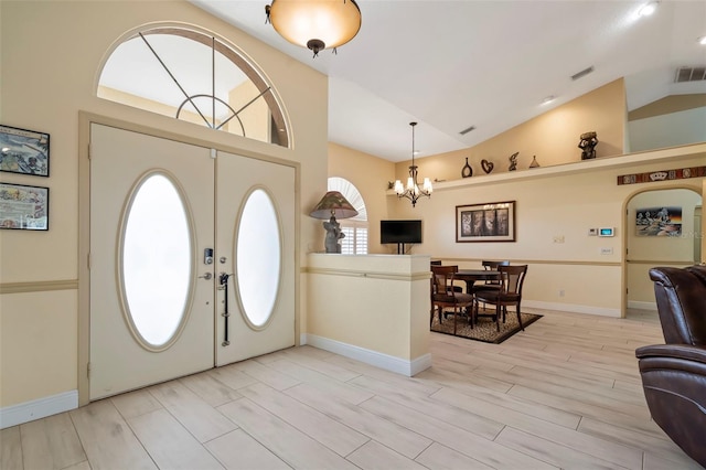 foyer entrance with lofted ceiling, an inviting chandelier, light wood-style flooring, and visible vents