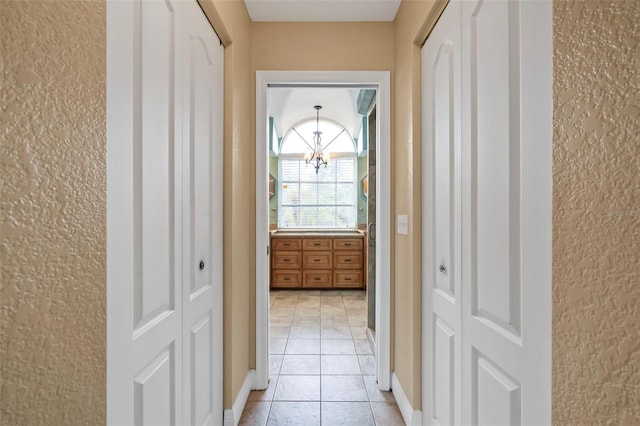 corridor featuring light tile patterned floors, baseboards, and an inviting chandelier