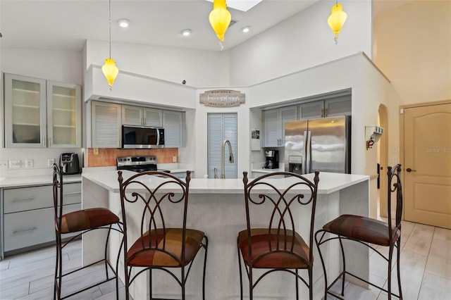 kitchen featuring light countertops, appliances with stainless steel finishes, glass insert cabinets, and pendant lighting