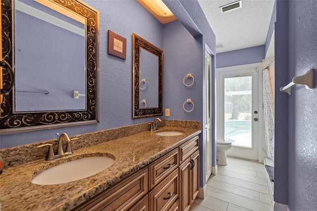 bathroom with visible vents, a sink, toilet, and double vanity