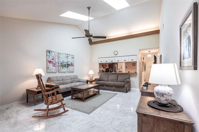 living room featuring ceiling fan, high vaulted ceiling, a skylight, baseboards, and marble finish floor