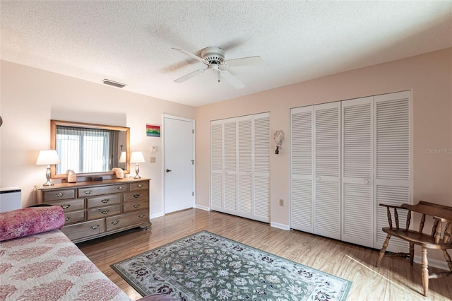 bedroom featuring two closets, visible vents, a ceiling fan, wood finished floors, and baseboards