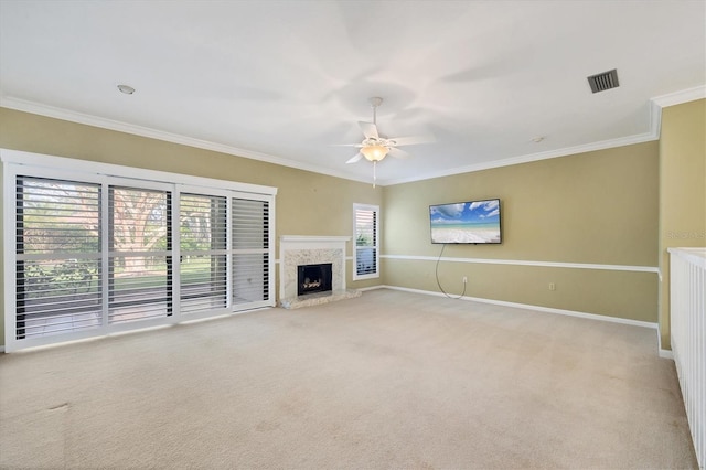 unfurnished living room featuring ceiling fan, crown molding, a high end fireplace, and light colored carpet