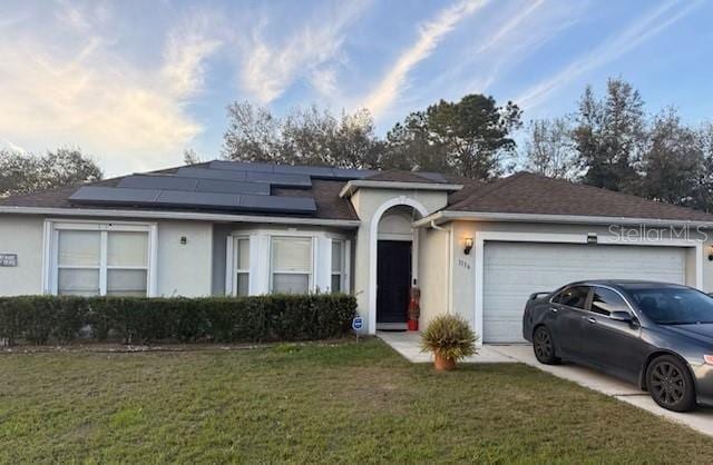 single story home featuring solar panels, concrete driveway, an attached garage, a front lawn, and stucco siding