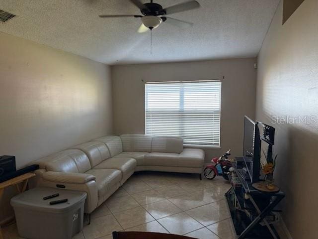 living room featuring light tile patterned floors, a textured ceiling, visible vents, and a ceiling fan