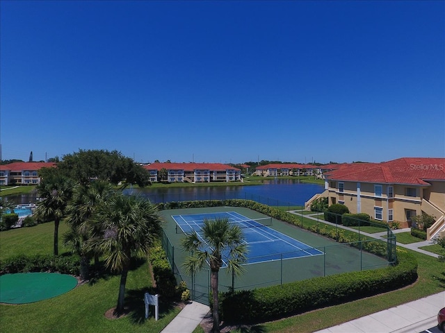 view of tennis court featuring a water view, a residential view, fence, and a yard