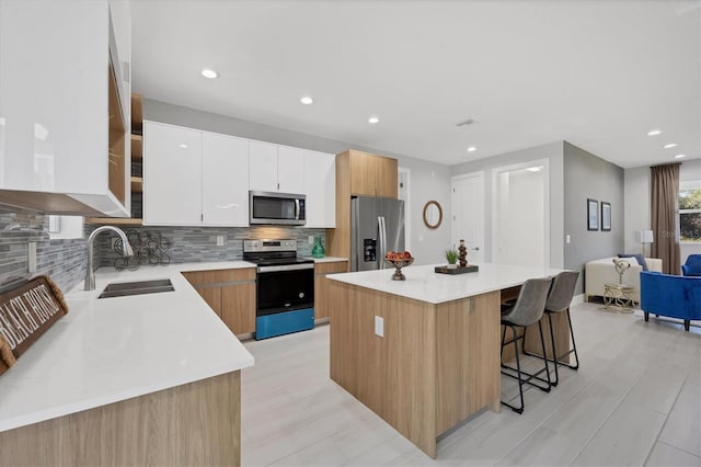 kitchen with a sink, white cabinets, light countertops, appliances with stainless steel finishes, and a center island