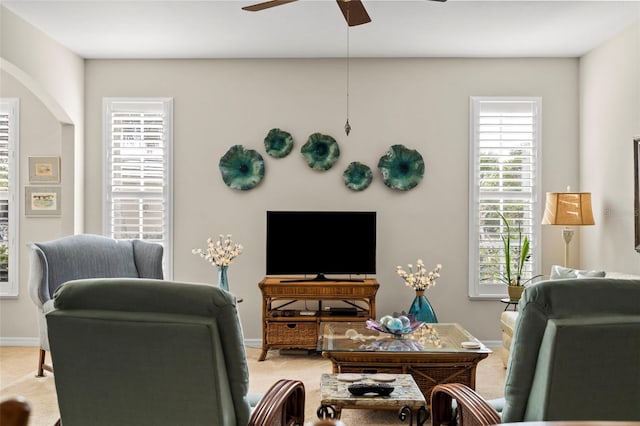 carpeted living room with baseboards, arched walkways, and ceiling fan