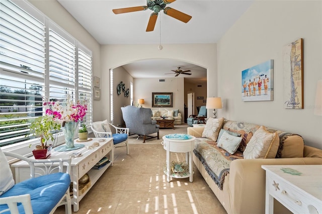 living area featuring light tile patterned floors, visible vents, arched walkways, and ceiling fan