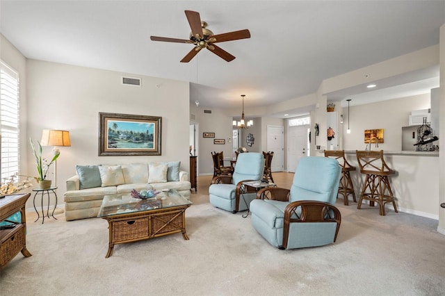 carpeted living area with ceiling fan with notable chandelier, baseboards, and visible vents