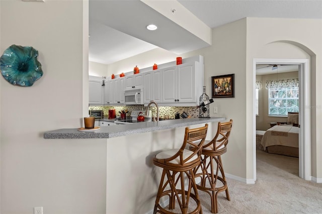 kitchen featuring backsplash, light colored carpet, a kitchen bar, a peninsula, and white appliances