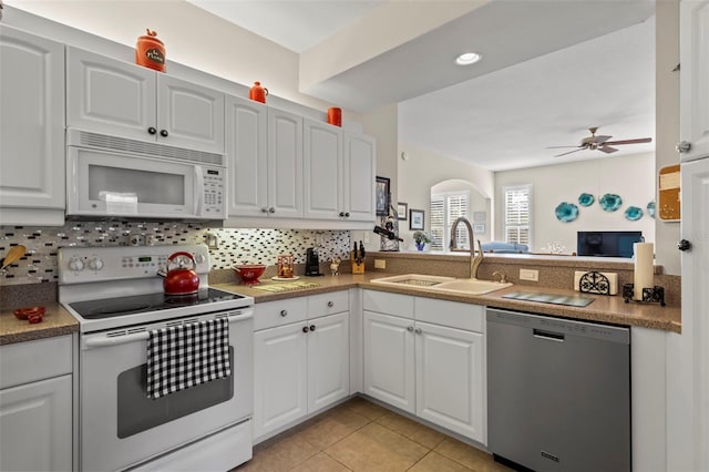 kitchen featuring light tile patterned floors, decorative backsplash, white appliances, white cabinetry, and a sink