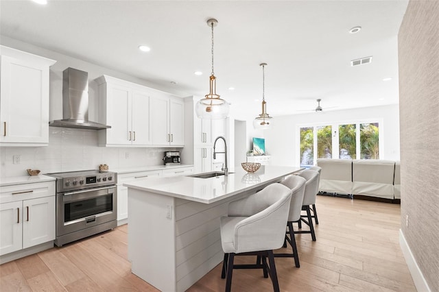 kitchen featuring light wood finished floors, high end stainless steel range, wall chimney range hood, and a sink