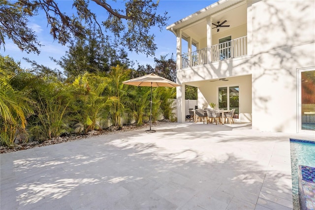 view of patio / terrace featuring a balcony, a ceiling fan, fence, outdoor dining area, and a swimming pool