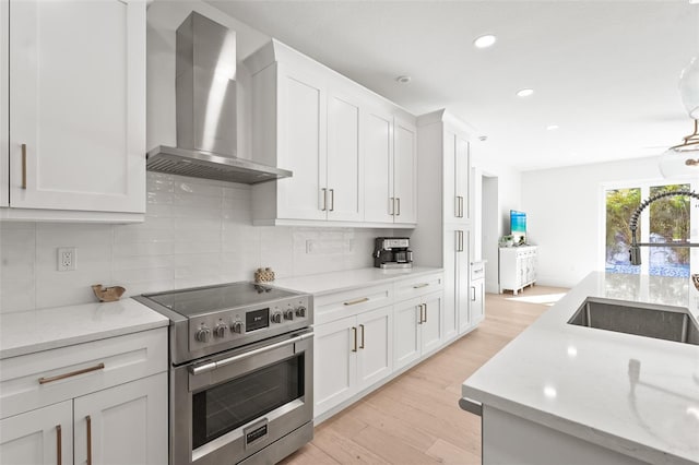 kitchen featuring stainless steel range with electric stovetop, backsplash, light wood-style floors, wall chimney exhaust hood, and white cabinets