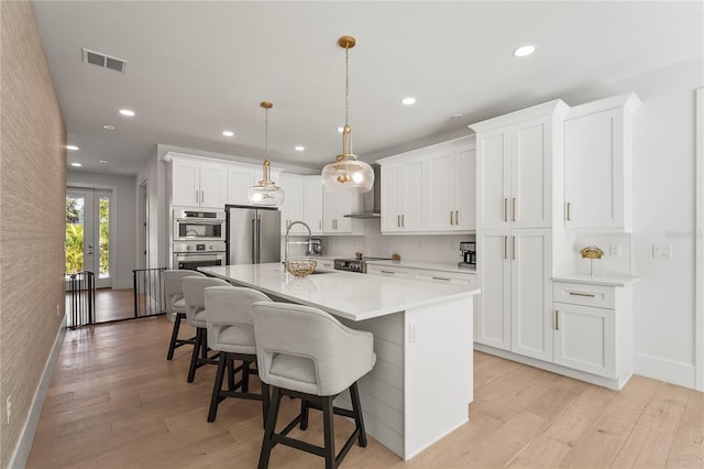 kitchen featuring visible vents, a kitchen island, a breakfast bar, appliances with stainless steel finishes, and light wood-style floors