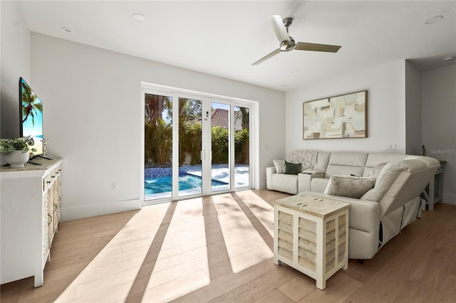 living area featuring baseboards, ceiling fan, and light wood finished floors