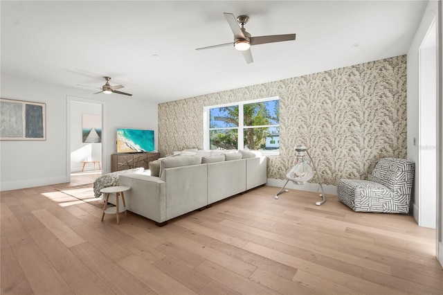 living room with wallpapered walls, baseboards, light wood-type flooring, and a ceiling fan