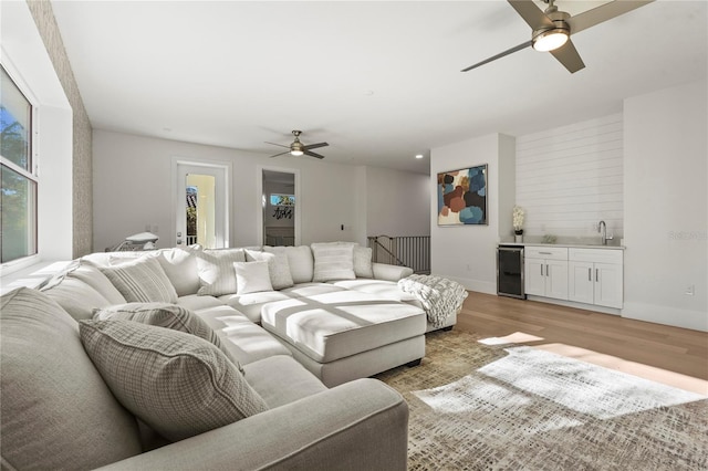 living area with beverage cooler, a ceiling fan, light wood-style floors, indoor wet bar, and baseboards