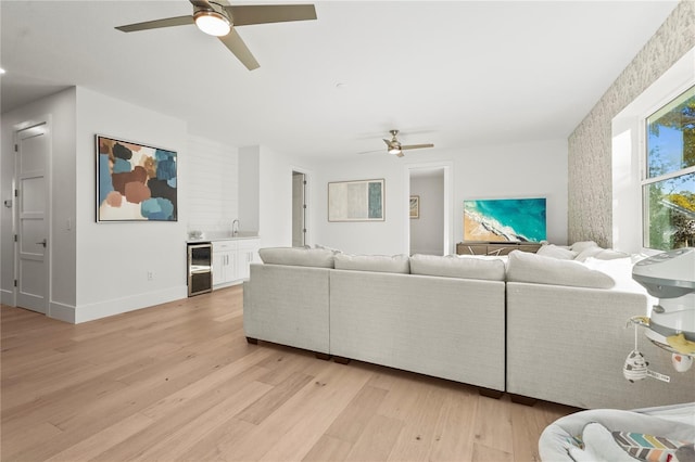 living room featuring ceiling fan, light wood-type flooring, baseboards, and beverage cooler