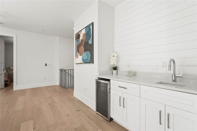 bar featuring wine cooler, light wood-style flooring, baseboards, and a sink