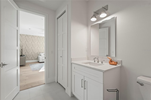 half bath featuring vanity, baseboards, wallpapered walls, tile patterned floors, and toilet